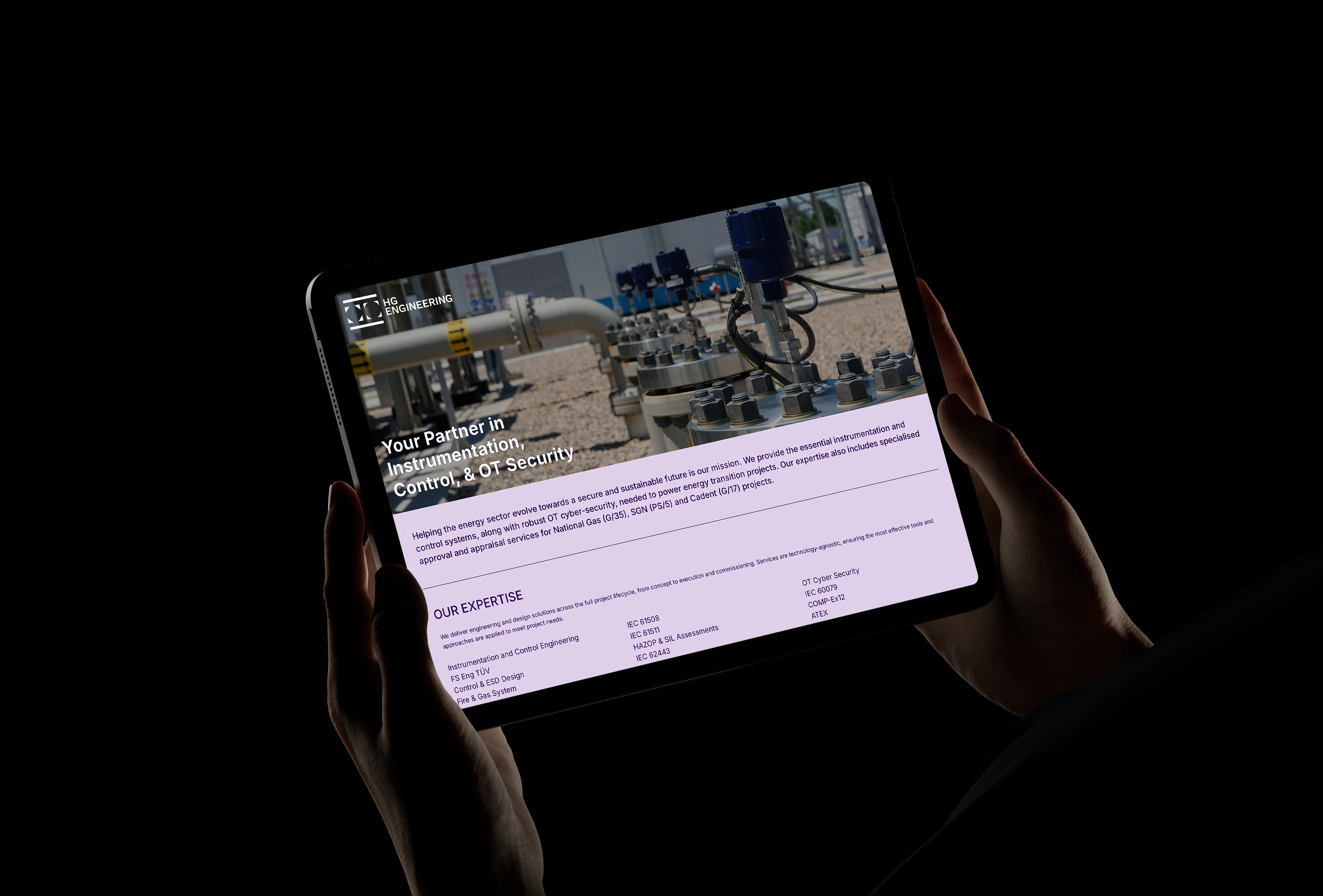 Hands holding a tablet showing the responsive tablet layout of the HG Engineering homepage.